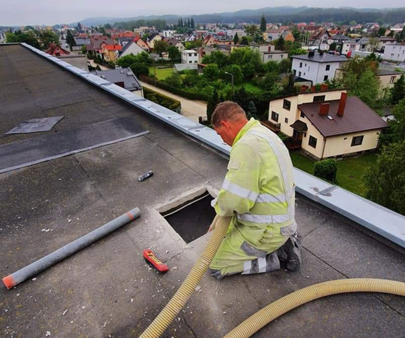 Mężczyzna wlewa wełnę celulozową prez dach